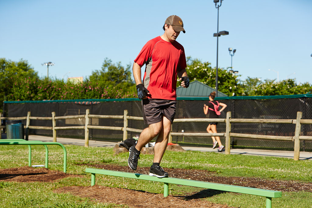 man balances on balance beam at outdoor gym